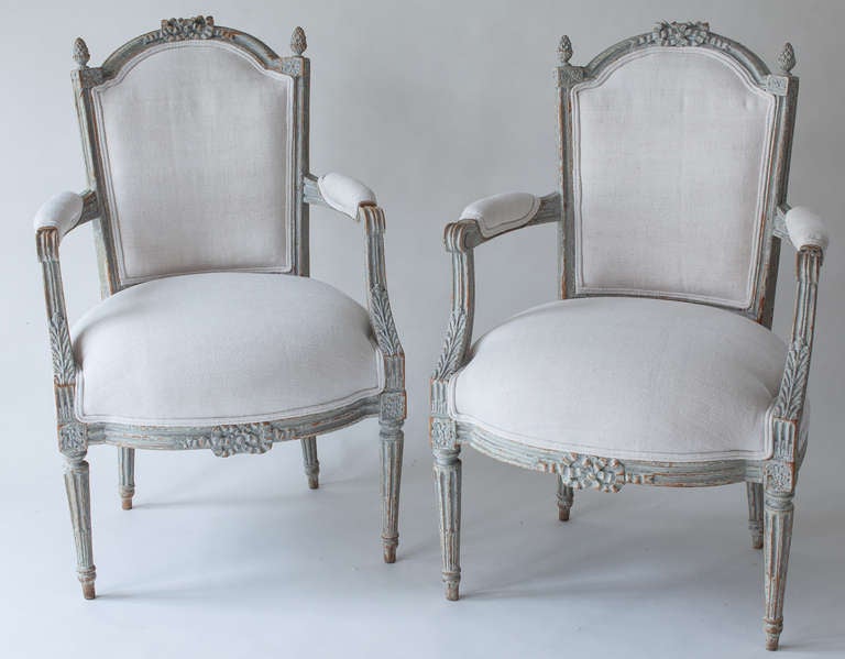 A elegant pair of Louis XVI style armchairs with delicate bow carvings on the back and apron and finials typical of that style. The pale bluish paint is original. New upholstery with a French late 19th century linen fabric.