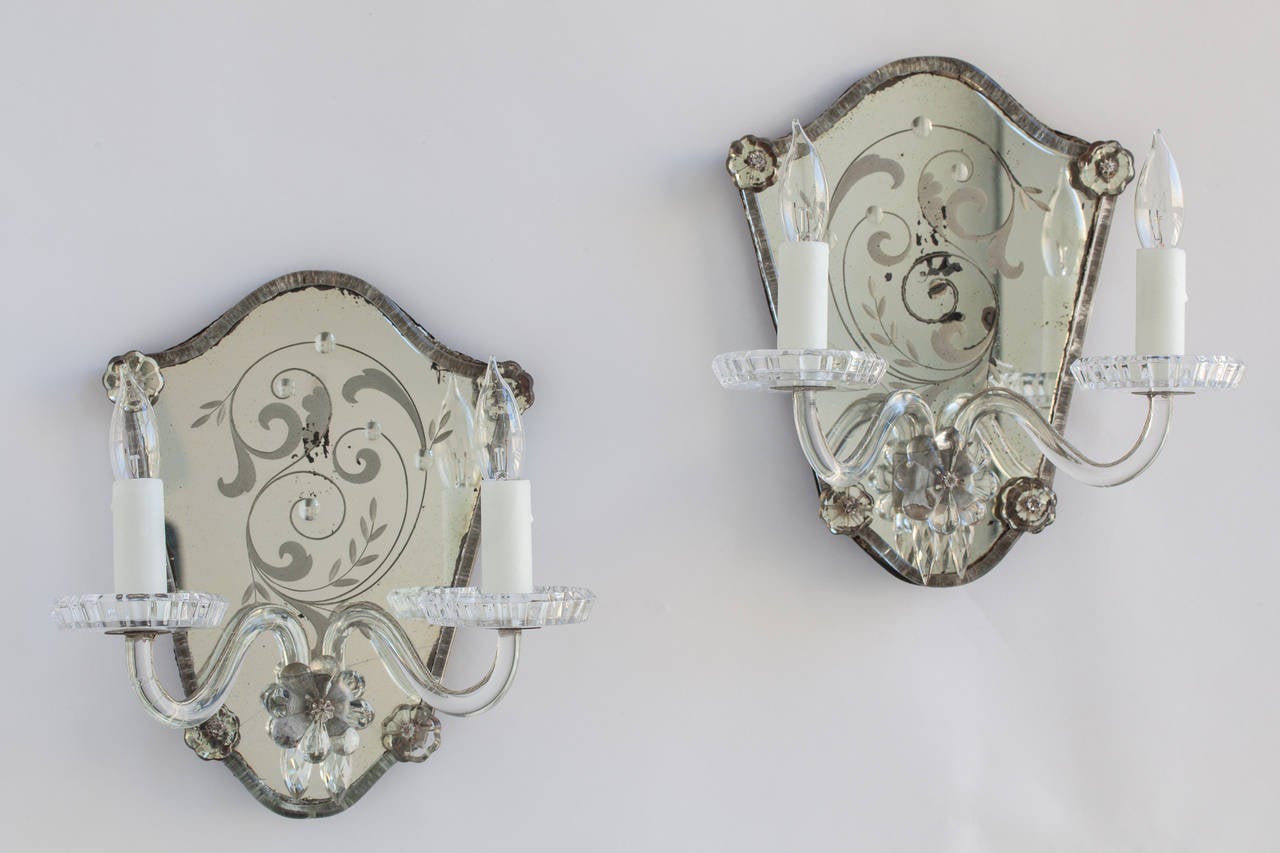 This very special pair of French mirrored sconces with curving leaves etched on the glass are encircled with glass tubing punctuated by crystal flowers. The two clear glass tubular arms leading to the lights emerge from a central crystal flower. The