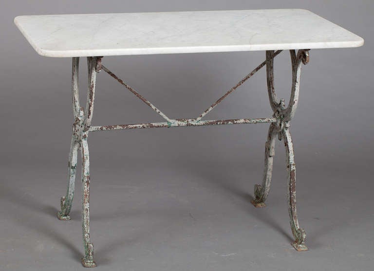 A great example of a French bistro table from the 19th century with an ornate cast iron base bearing traces of old green paint. A classic French medallion embellishes the cross of the legs and a rod going across the middle adds stability. The marble