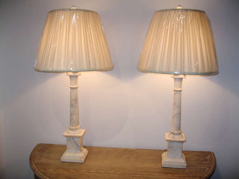 A pair of marble lamps on a stepped base with elaborate carved acanthus leaf topped column. Marble has excellent veining and is a nice clear shade of off white with no discolorations. The lamps are in perfect condition and come with new pleated