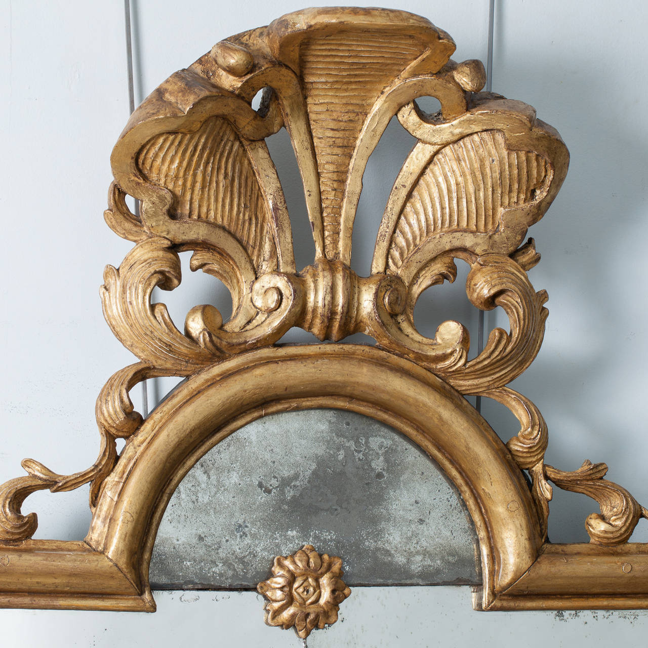 This elegant Louis XVI period mirror with original water gliding and old glass has a magnificent gilded fleur-de-lis at the top positioned above a curved center arch. Three gilded medallions mark the six sections of the divided mirror with a curved