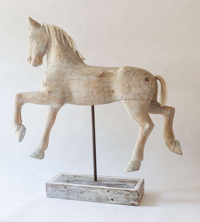 A beautifully carved Swedish horse on stand with its original mane and tail. It has been scraped to reveal traces of the original paint surface. The horse gives the impression of graceful movement with delicate legs and hooves captured in the air.