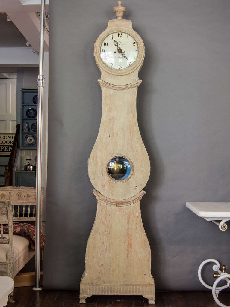 A Swedish tall case clock in the traditional Mora style. The face is signed by the maker N. Lundgren and the bonnet is topped with a carved urn. The clock has an interesting movement which includes a separate minute dial as well as an alarm, grey or