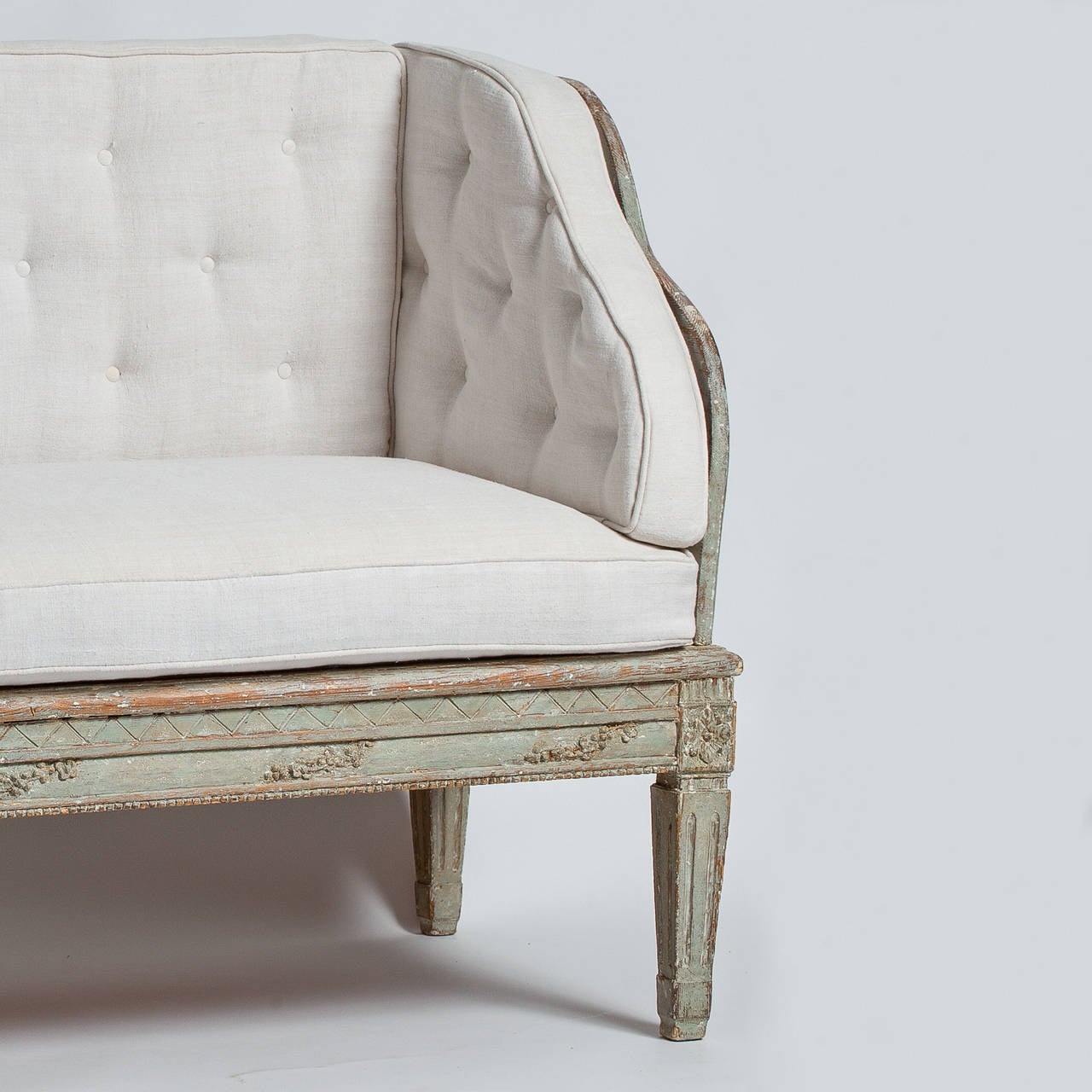 This Swedish, Gustavian period "Trågsoffa" retains the original pale blue paint surface with carvings of flowers on the base rail and flower medallions above reeded legs. It has been upholstered in a linen fabric in the original style,