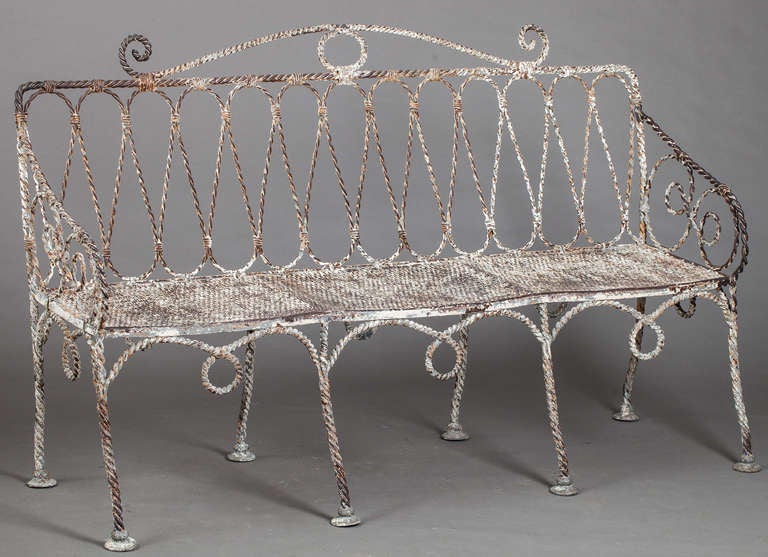 A French iron garden bench with intricate rope motif and elaborate scroll details. The openwork metal seat is divided into three sections and is in great condition. The piece retains much of the original white painted surface but has a very special