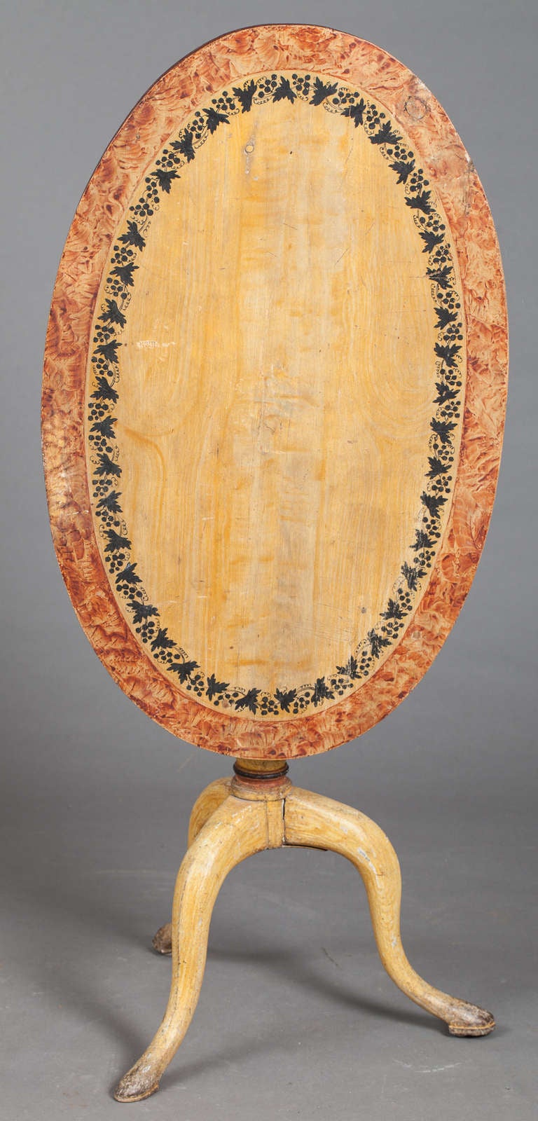 A charming Swedish oval flip-top table, circa 1840. The original painted surface is a light golden color with a band of painted grape leaves suggesting that it may have been a wine tasting table. The outer edge is faux painted in a contrasting rust