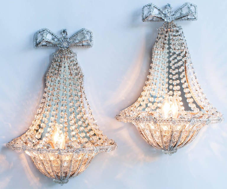 A charming pair of French crystal sconces backed by a mirror with a bow at the top descending to a graceful basket shape. The sconces have been newly electrified for U.S circuits and have one light each which, when reflected in the mirror, gives