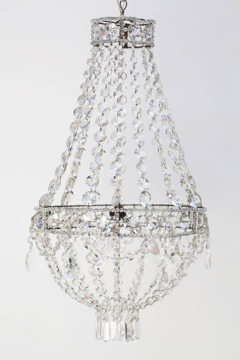 An elegant French crystal chandelier that has a simple teardrop shape of round cut crystals framed by large drop crystals on the outside rim. Crystal pendants at the bottom surround a small crystal ball. This piece has three interior lights and has