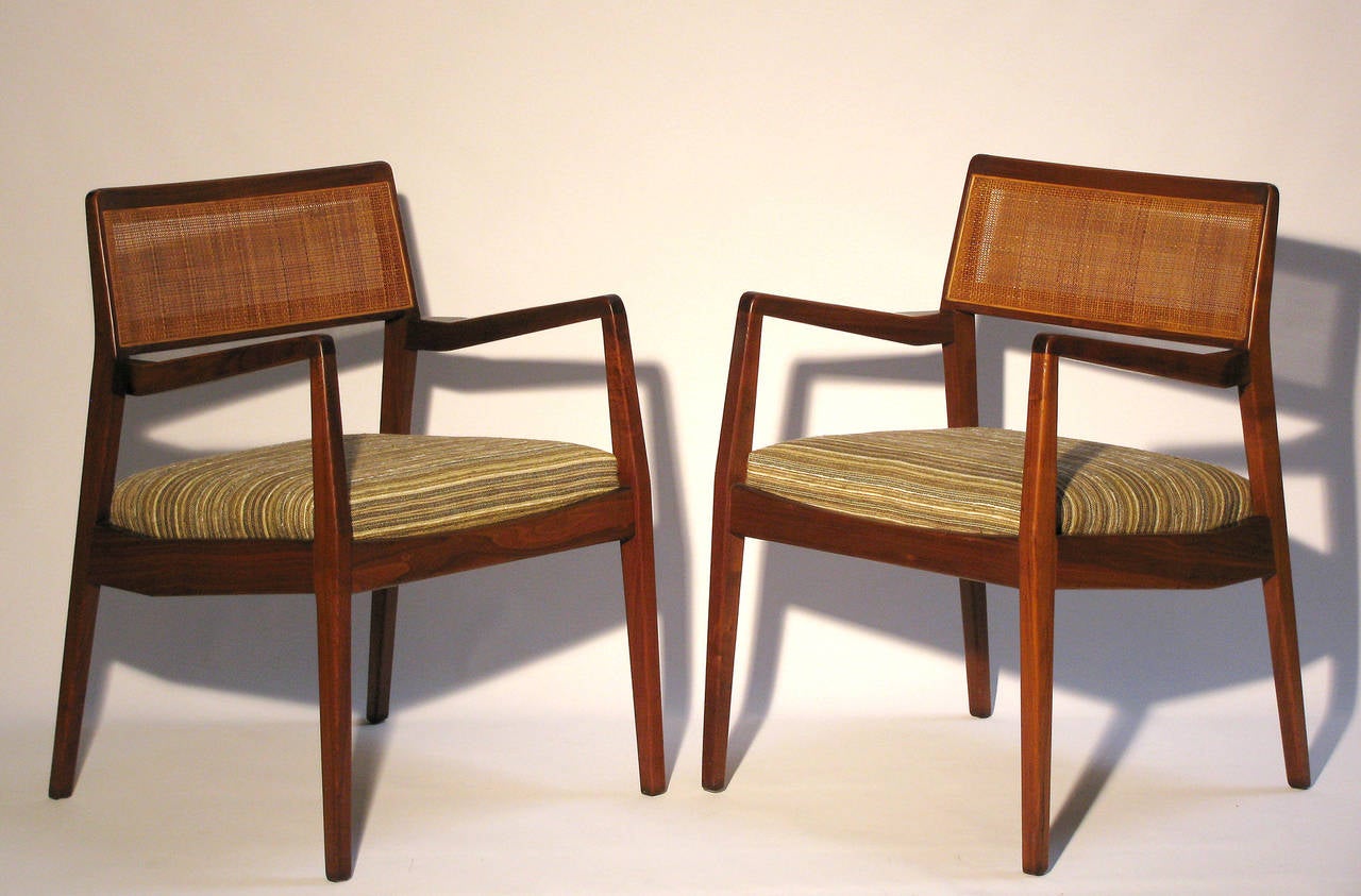 A pair of Jens Risom “Playboy” C140 chairs in walnut. The chairs have been reupholstered with an earthy striped wool-linen fabric. A sleek design with original cane backs, curved arms and slightly tapered legs. This chair is nick-named 'the Playboy'