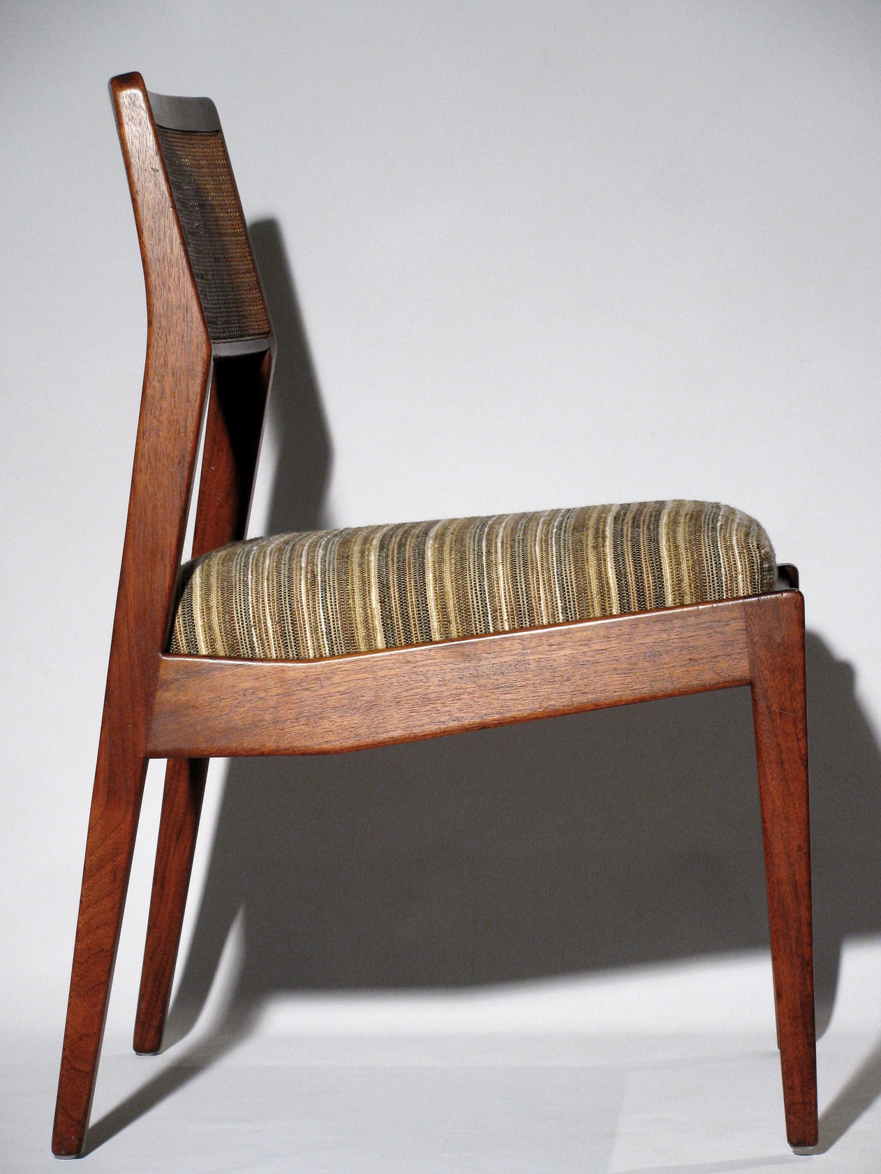 A set of four Jens Risom “Playboy” side chairs in walnut. The chairs have been reupholstered with a earthy striped wool-linen fabric. A sleek design with original cane backs, angular lines, and slightly tapered legs. This chair is nick-named 'the