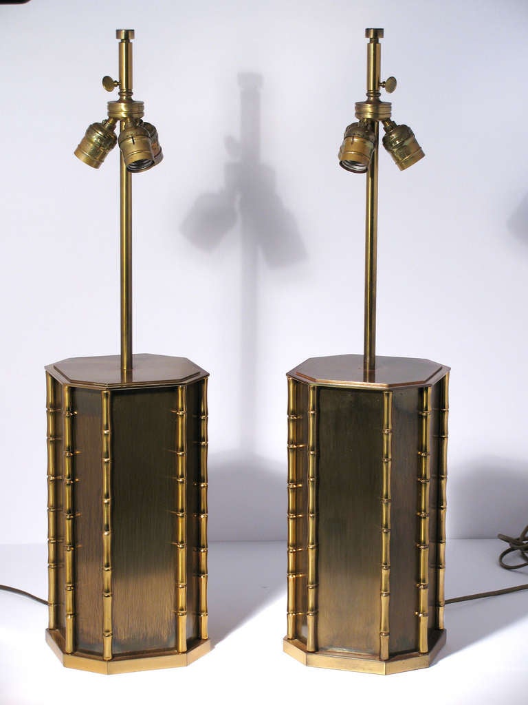 Pair of chic bronze and brass table lamps by Maison Charles, France. The lamps are a octagon-form design of patina finish panels, trimmed with polished bamboo reeds. They retain their original silk and brass frame shades. European wiring with switch
