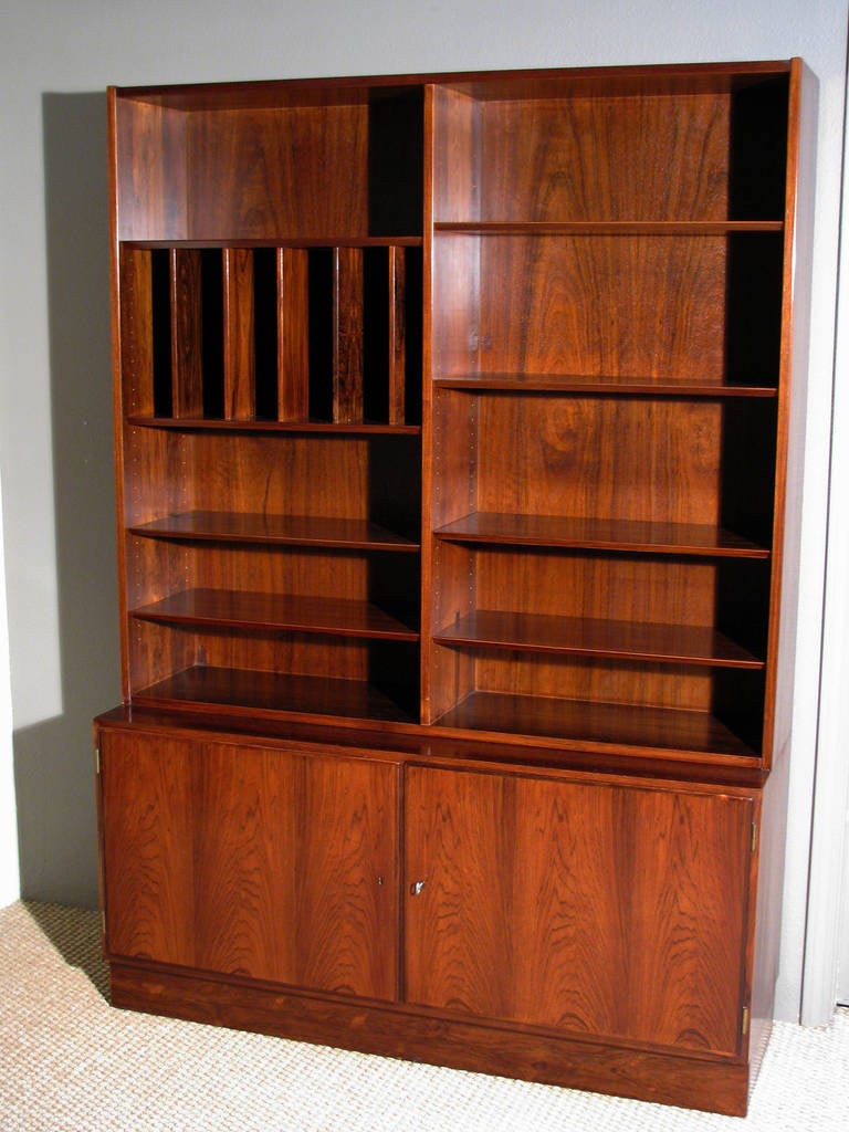 A beautiful Danish modern bookmatched grain rosewood bookcase with six adjustable shelves and five adjustable vertical shelves; the whole resting on a storage cabinet with locking doors, brass escutcheons. The doors open to a beautiful sycamore