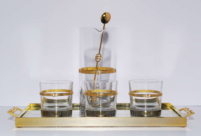 A rare and fabulous GUCCI martini bar set trimmed with gilt gold and silver metal serving tray, three cocktail glasses, carafe and stirrer; Six pieces total. The glass carafe and cocktail glasses are most likely Barovier glass and each piece is