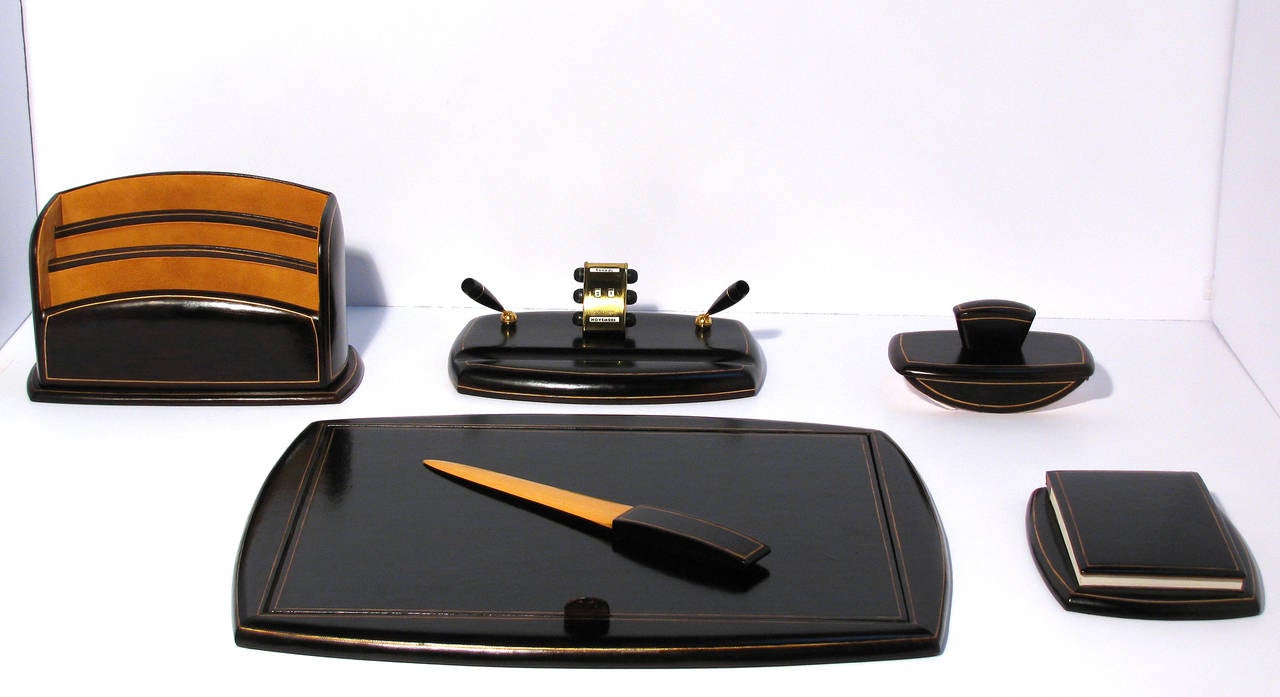A stunning six-piece leather desk of deep chestnut leather with gold gilt mounted border. Set features a removable writing pad inside the desk blotter, double pen holder, calendar, ink blotter, letter caddy, letter opener, and a note pad. Calendar