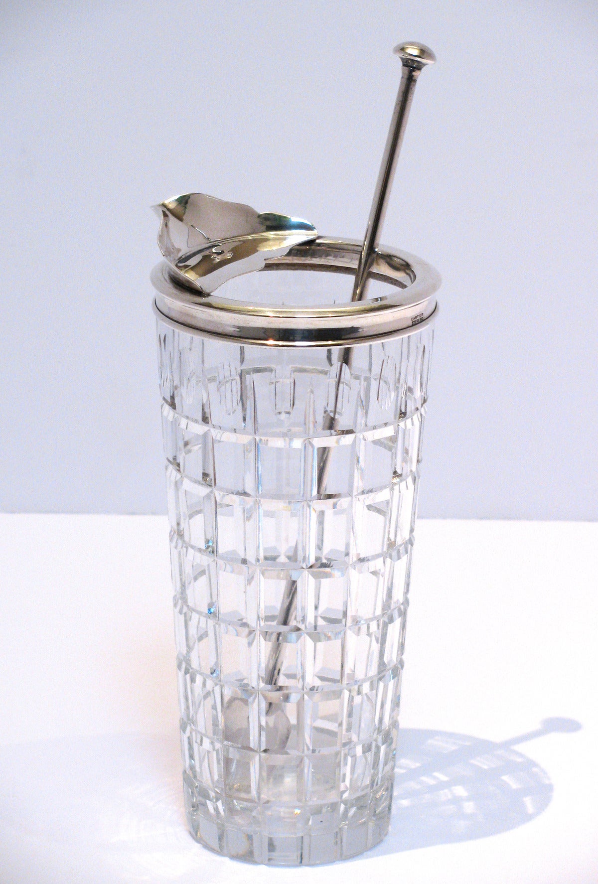 A cut crystal and sterling silver martini carafe with a sterling stirrer, by Cartier. Carafe is signed on silver rim, Cartier and has an etched hallmark on crystal base. Spoon stirrer is marked sterling.