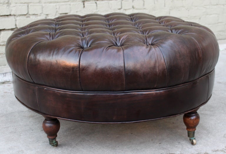 Leather tufted ottoman standing on four legs with casters.