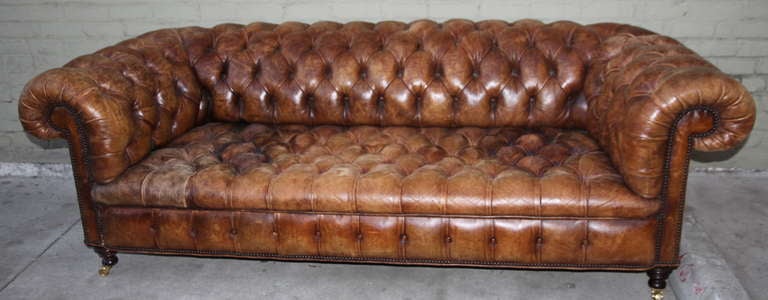 English leather tufted Chesterfield Sofa with nailhead trim detail. The sofa stands on ebony colored feet with brass casters.