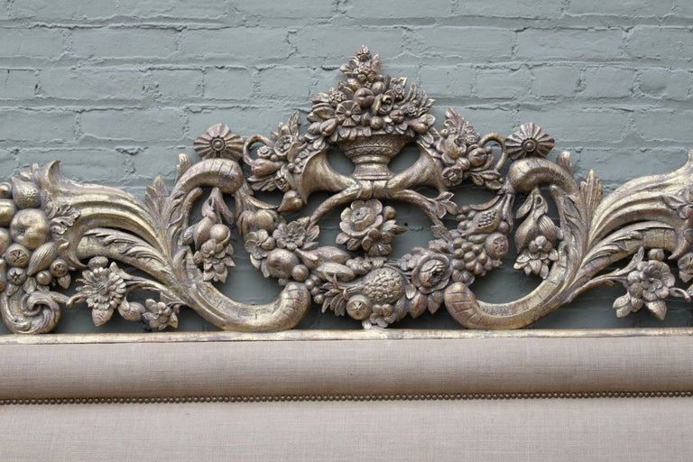 Stunning custom burlap upholstered headboard with 19th century 22K giltwood architectural piece with fruit, cornucopias, acanthus leaves, and flowers at the top with brass nailhead trim detail throughout.
