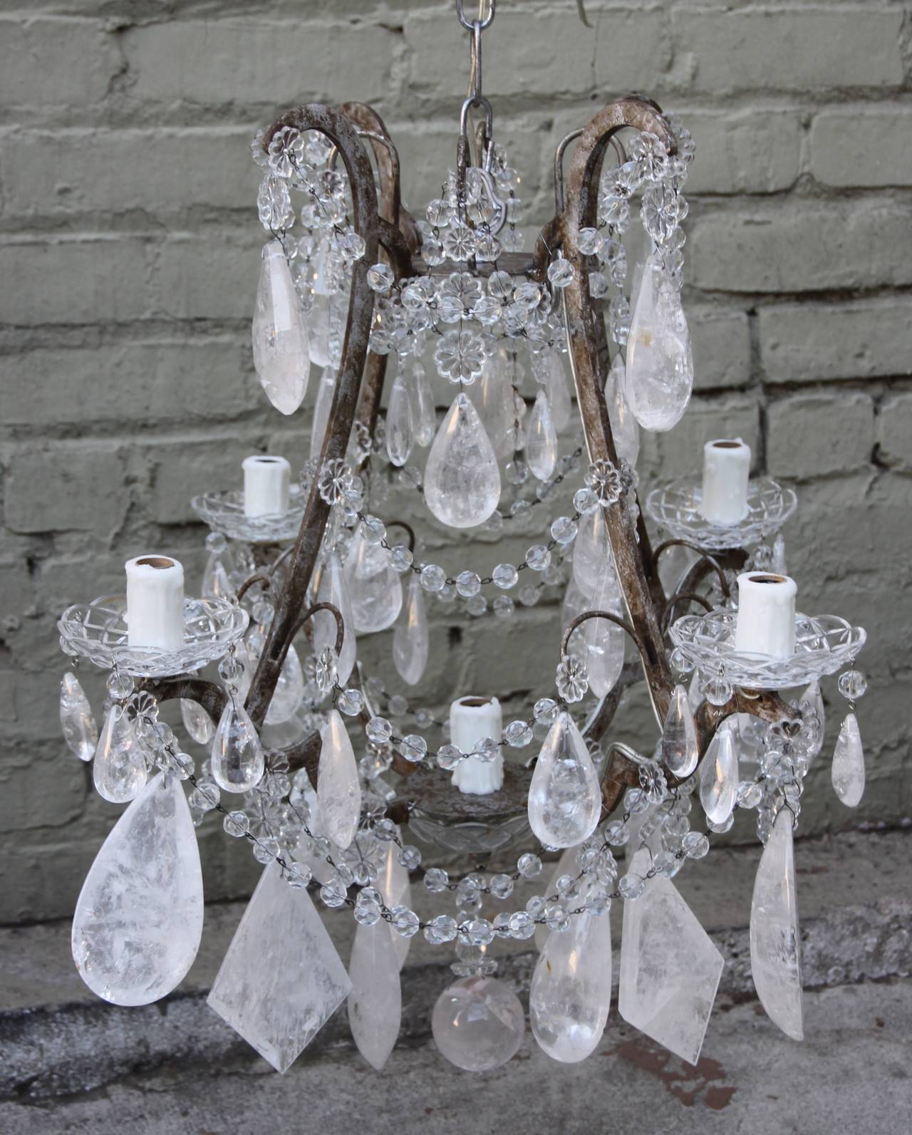 Five-light chandelier adorned with both tear drop and diamond-shaped rock crystals in varying sizes on a distressed silver finished frame. A rock crystal ball hangs from the bottom of the fixture. Newly wired with wax candle covers and in working