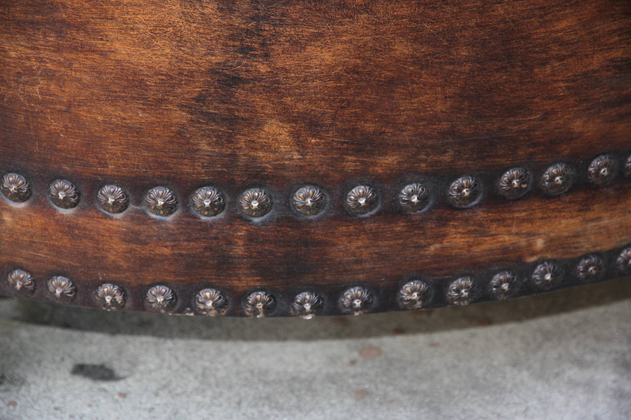 Leather tufted round ottoman standing on four bun feet with two rows of flower nailhead trim detail.