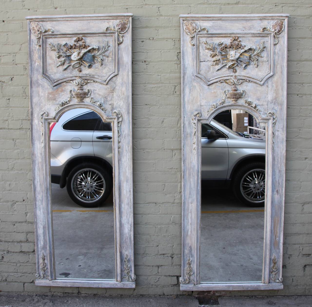 Pair of 19th century carved French painted mirrors with musical instruments flanked by acanthus and laurel leaves. Gold leaf highlights.