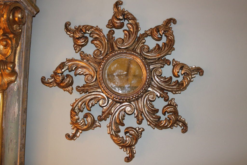 Petite carved Italian silver-leaf sunburst mirror.  The sun rays are shaped from carved scrolled acanthus leaves.  The mirror is slightly antiqued.  This mirror could work in any decor.