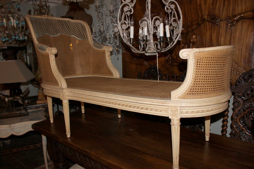 The arched stepped ribbon carved crestrail continuing to padded mounded down scrolled arms enclosing a caned back and conforming opposing end, over an oval seat, raised on tapered stop fluted legs ending in toupie feet. Provenance: Purchased