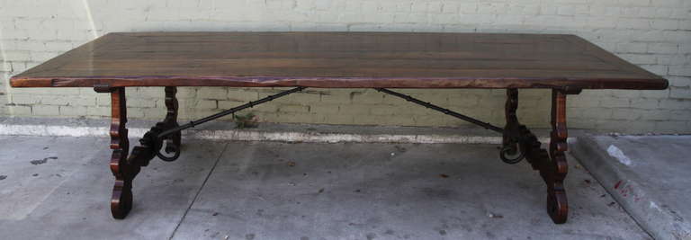 Spanish Baroque style walnut trestle table. The rectangular plank top above shaped supports and a wrought-iron stretcher.