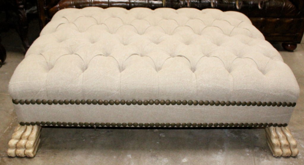 Newly upholstered tufted Belgium linen ottoman with carved faux painted paw feet and a double row of antique colored brass nail head trim detail.