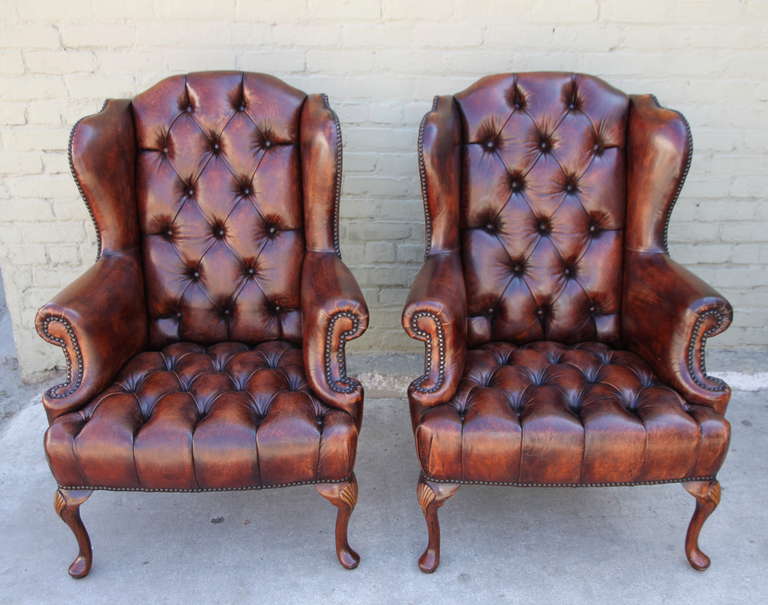 Pair of French distressed leather tufted wingback armchairs with cabriole legs and nailhead trim detail.