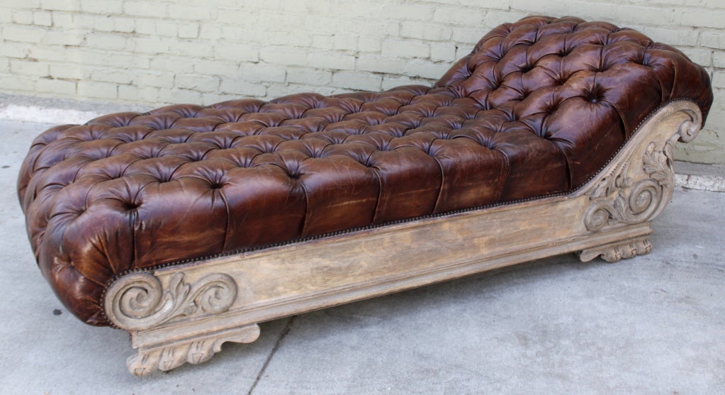 Leather tufted chaise longues with weather carved frame and nailhead trim detail.