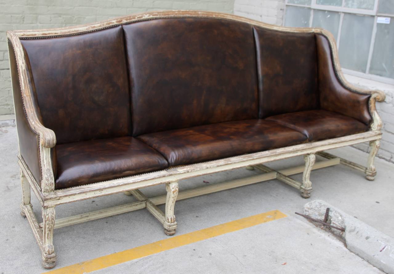 Eight legged French upholstered leather painted bench with distressed brown leather and finished in nailhead trim detail.