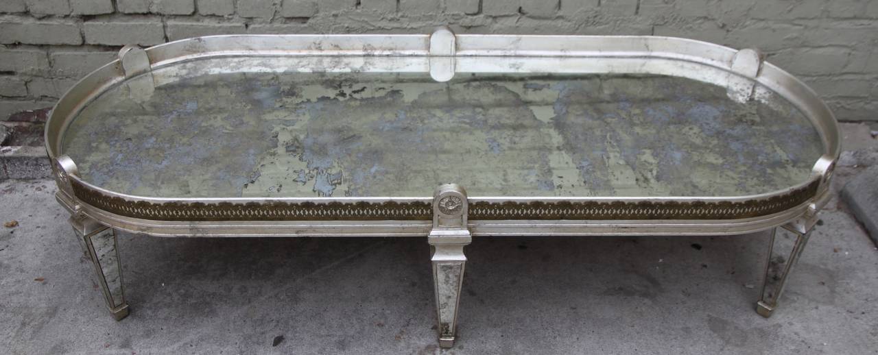 Silvered racetrack shaped coffee table with antique mirrored top standing on six mirrored legs.