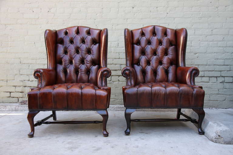 Pair of handsome English Georgian style leather tufted armchairs with cabriole legs and bottom stretcher. Antique brass nail head trim detail.