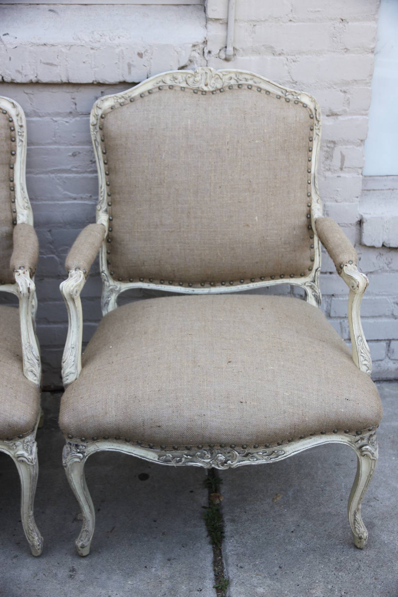Pair of French cream colored Louis XV style painted fauteuils newly upholstered in burlap textile with nailhead trim detail. Back are upholstered in painted cane.