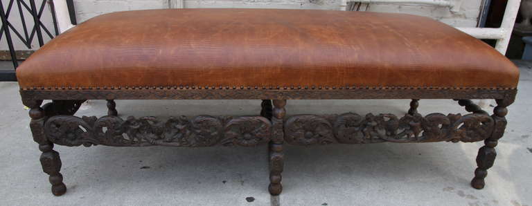 Spanish Baroque style walnut carved bench standing on six legs and upholstered in crocodile patterned leather with spaced nail head trim detail.   The bench has carved cherubs flanking eagles with swriling acanthus leaves throughout.