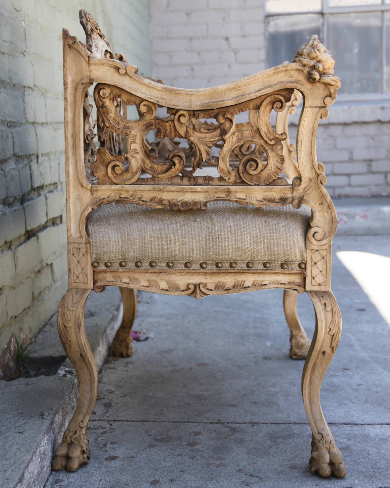 19th century Italian walnut bench with cherub faces and carved acanthus leaves though out. The bench is newly upholstered in burlap with self-welt and spaced nailhead trim detail.