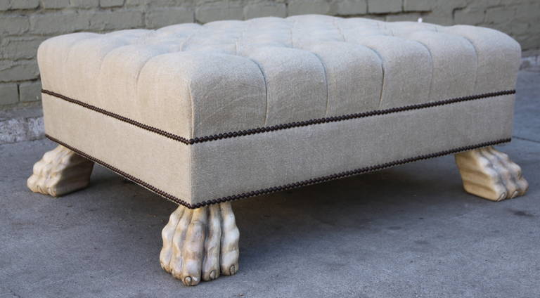 Custom tufted Belgium linen ottoman with double nailhead trim detail standing on four painted carved paw feet.