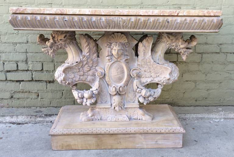 Italian carved wood washed walnut console with marble top. Console depicts a pair of griffins flanking a center cartouche with carved face and garlands of fruit.