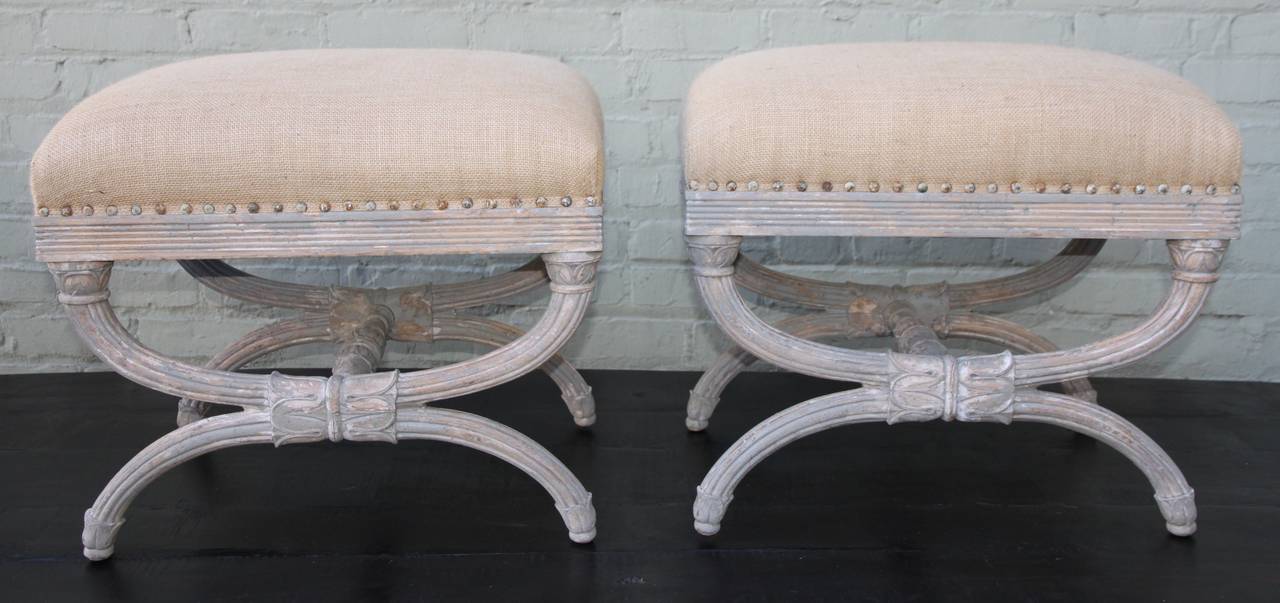 Pair of Italian X-frame painted benches with fluted legs and acanthus leaf detail. Newly upholstered in burlap textile with nailhead trim detail.