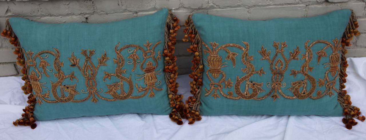 Pair of appliquéd turquoise linen pillows with tassel fringe at sides. Down inserts.