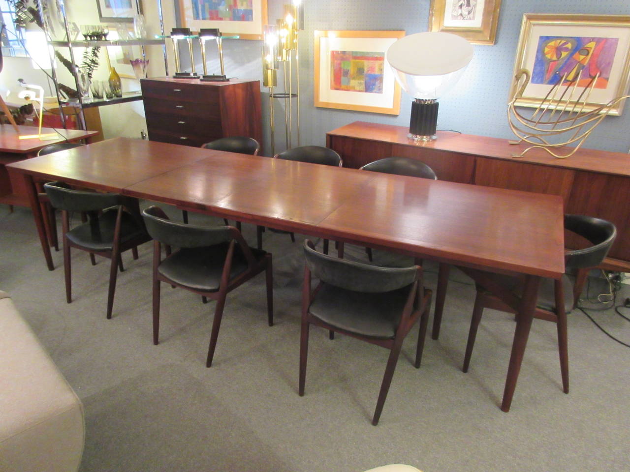 Very large table with two leaves and eight matching chairs bought in Denmark in the mid-1950s The table has three legs at either end joined by stretchers and has two large leaves with flattened pegs to join table. The table is 74.5 x 35.5 when