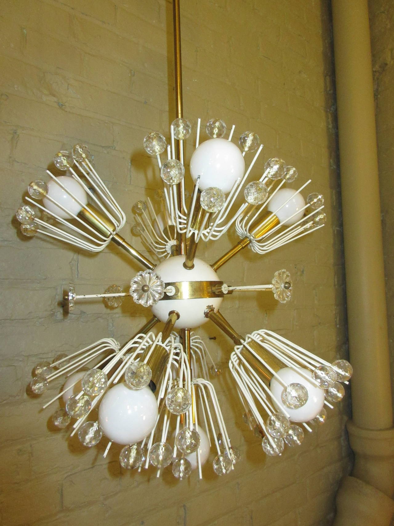 Ten starbursts make up this 1950s chandelier. Painted ivory and brass with glass balls on every other metal stem. Center brass ring is made up of six stems with glass flowers on end. Some paint loss on ivory painted parts.