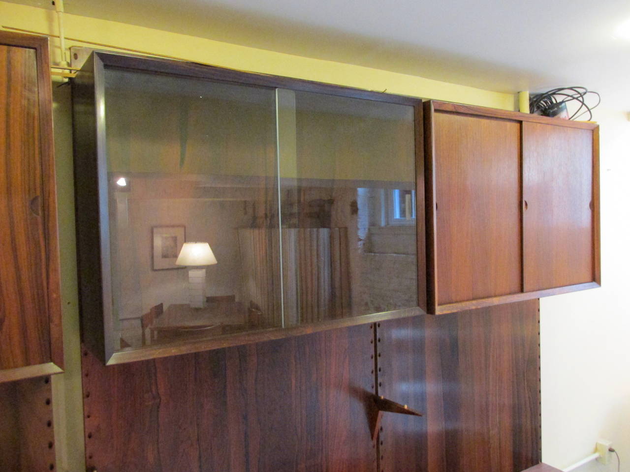 Large solid backed wall unit with six cabinets of sliding doors and drawers and two glass shelves. The back panels mount to the wall and cabinets and shelves are supported via angled wooden pegs. Several holes have been cut for electrical cords but