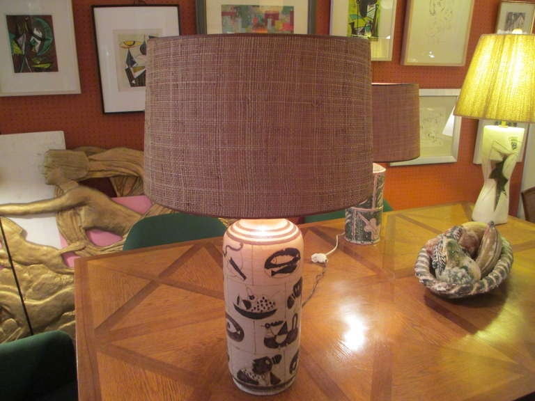 Large ceramic lamp with images of food, musical instruments, women and animals in shades of taupe and cream.  Signed on the bottom with typical Gambone donkey symbol.  Original lamp shade covered in split-woven bamboo.
