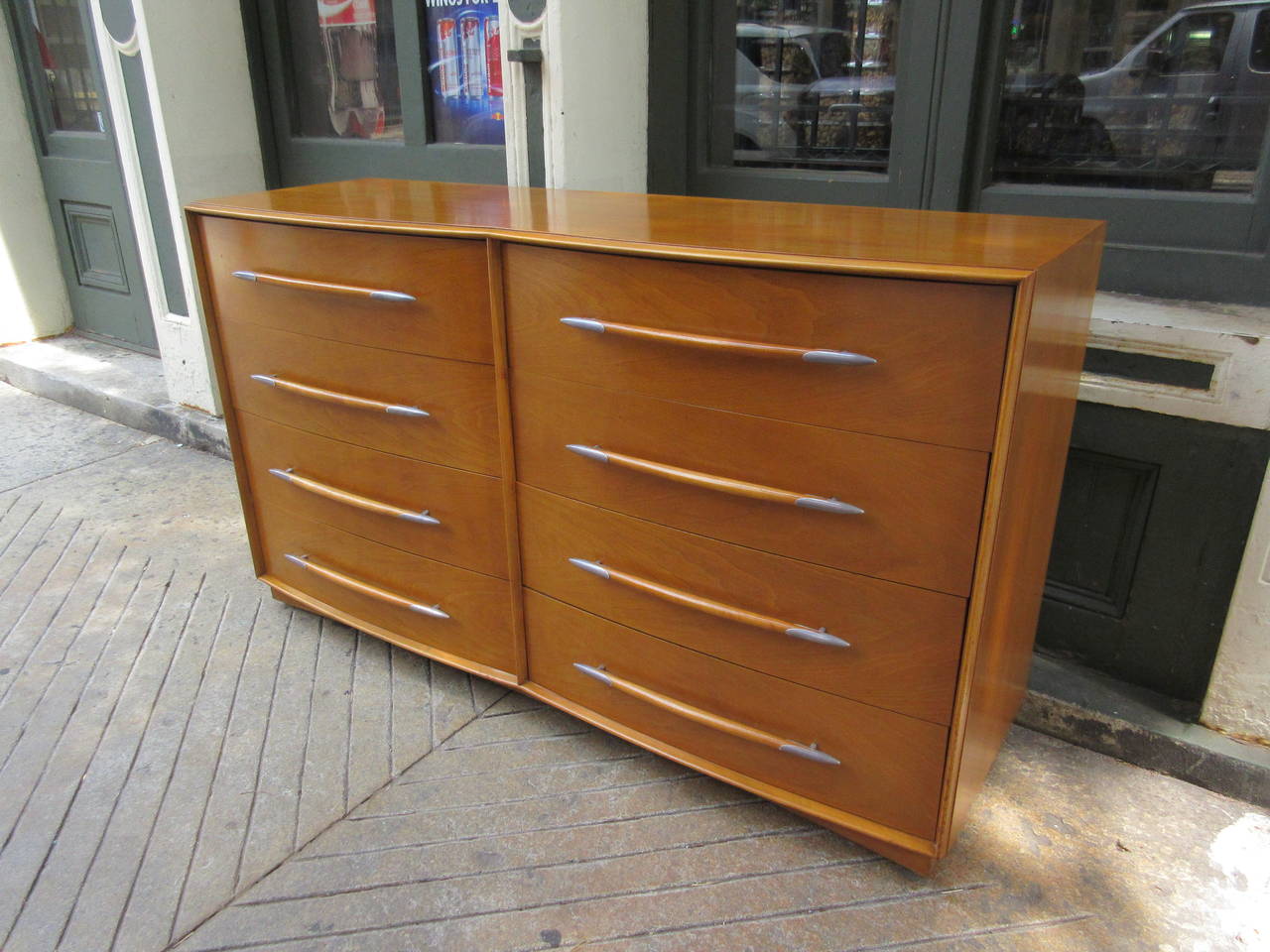 Part of a large bedroom set which is also available this chest has a double bank of four drawers made of a gently bowed plywood with a honey walnut veneer and solid walnut pulls capped in a metal holder. Set bought from original family and dated