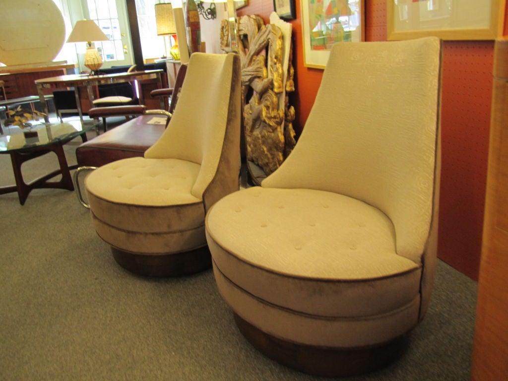 Pair of two tone swivel lounge chairs in a taupe velvet and a cream fabric with concentric rectangles on plinth of walnut with a self righting feature which brings these chairs back to a selected resting spot