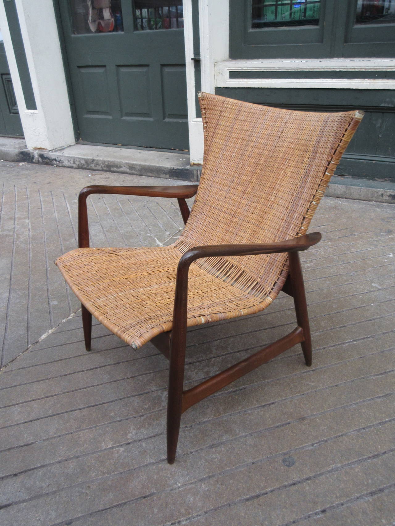 Interesting walnut framed chair with brass caps and steel tubing stretched with woven caning with exaggerated winged back. Chairs uses slot construction typical of the period.