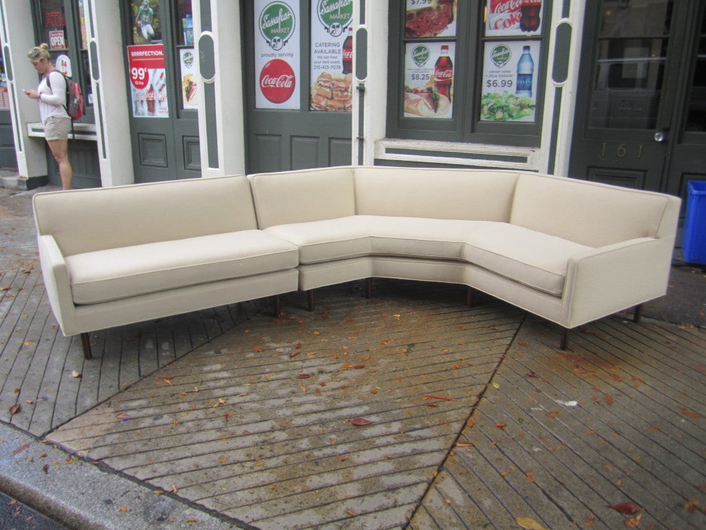 Just reupholstered (shown also with old original upholstery)in cream hopsack.  Two piece sectional with wrap-around walnut table with two drawers and brass trim. Table can be positioned several ways behind sofa. 150 inches listed is corner to corner