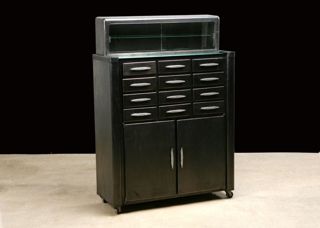 French Art Deco style Polished Metal Dentist Cabinet with 12 small drawers, each lined in glass, two door lower cabinet doors, and upper portion with sliding glass doors. On casters.